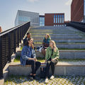 Four people sitting on the stairs near School of Business and Väre, in sunlight