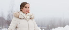 Heli Julkunen seisoo talvisessa maisemassa ja katsoo hymyillen pois kamerasta. Hänellä on päällään valkoinen talvitakki ja taustalla näkyy sumua, puita ja lumihankia.