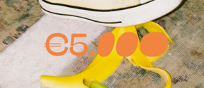 Close-up of a foot wearing a tennis shoe. The person is just about to step on a banana peel. In front, orange text reads €5000.
