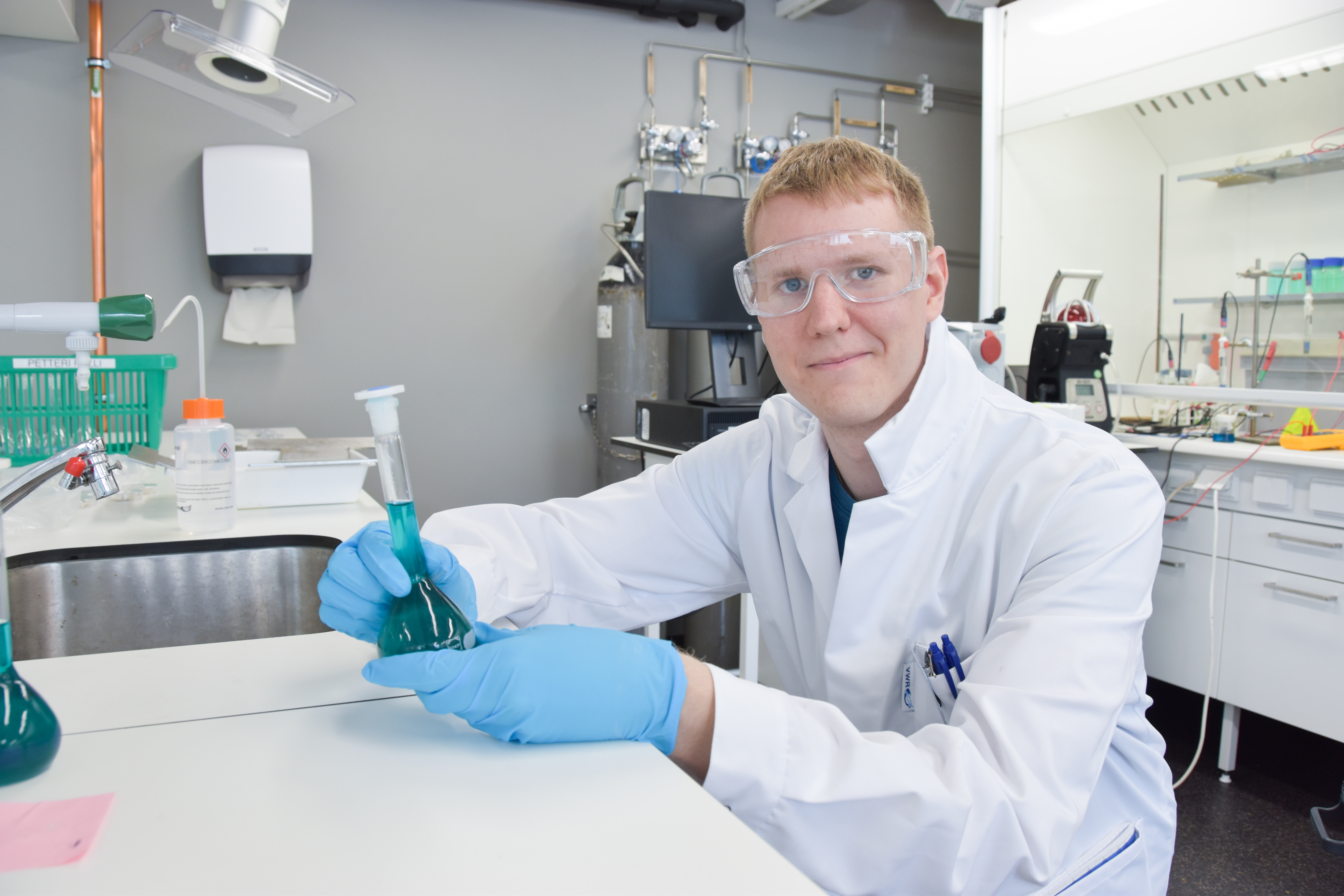 Jere in the laboratory with safety gear holding a bottle