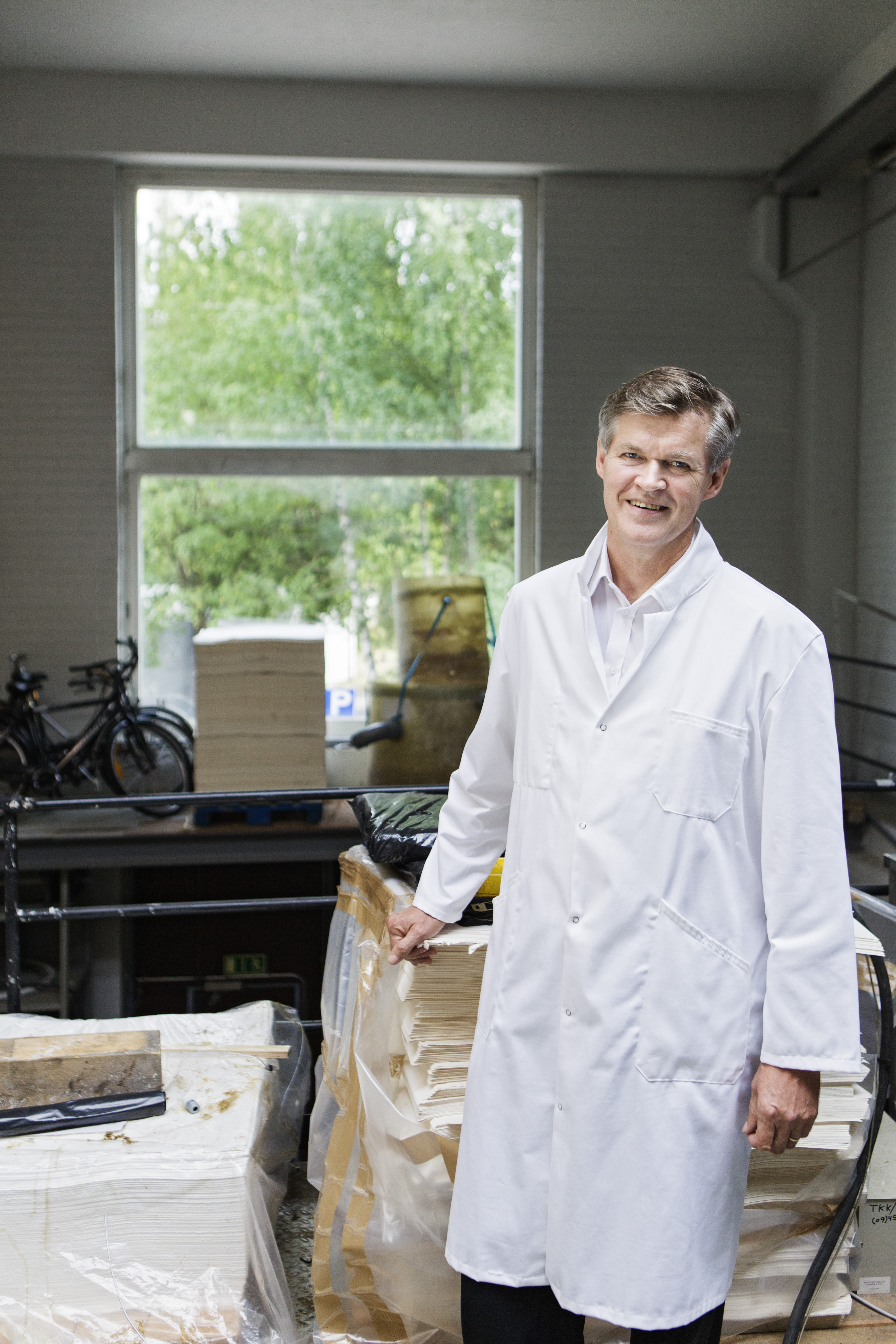 man standing in a storage in front of the window, wearing a white laboratory coat, smiling