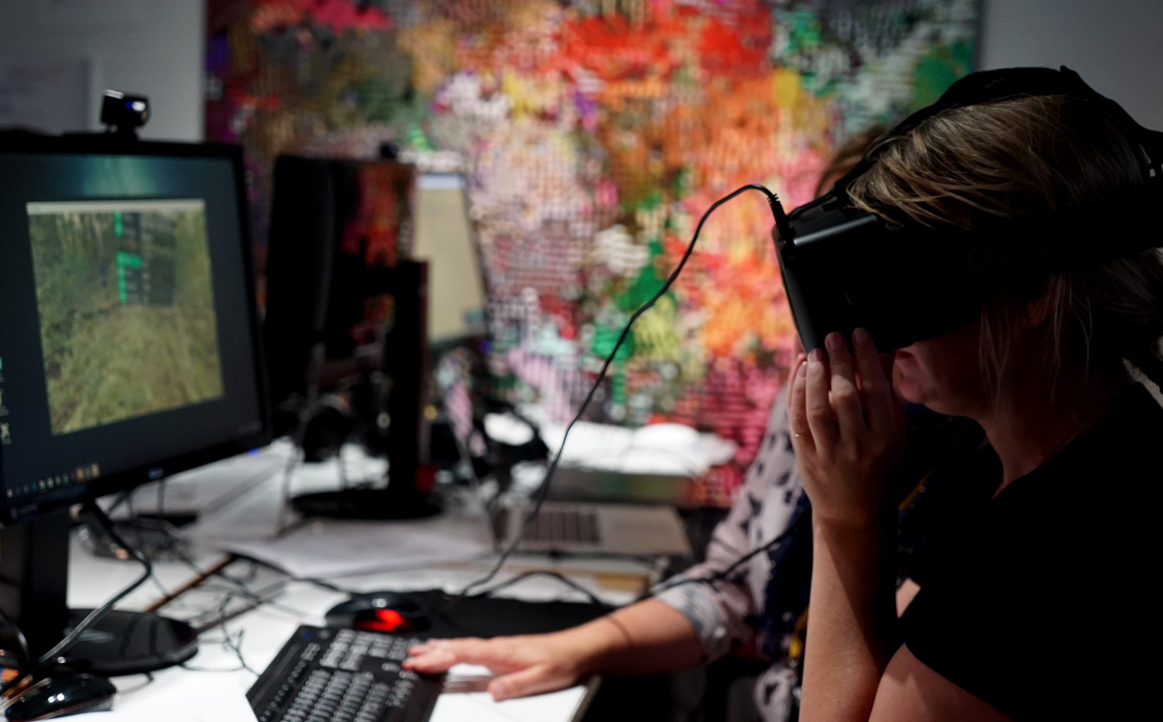 A person uses VR headset while another assists on the background