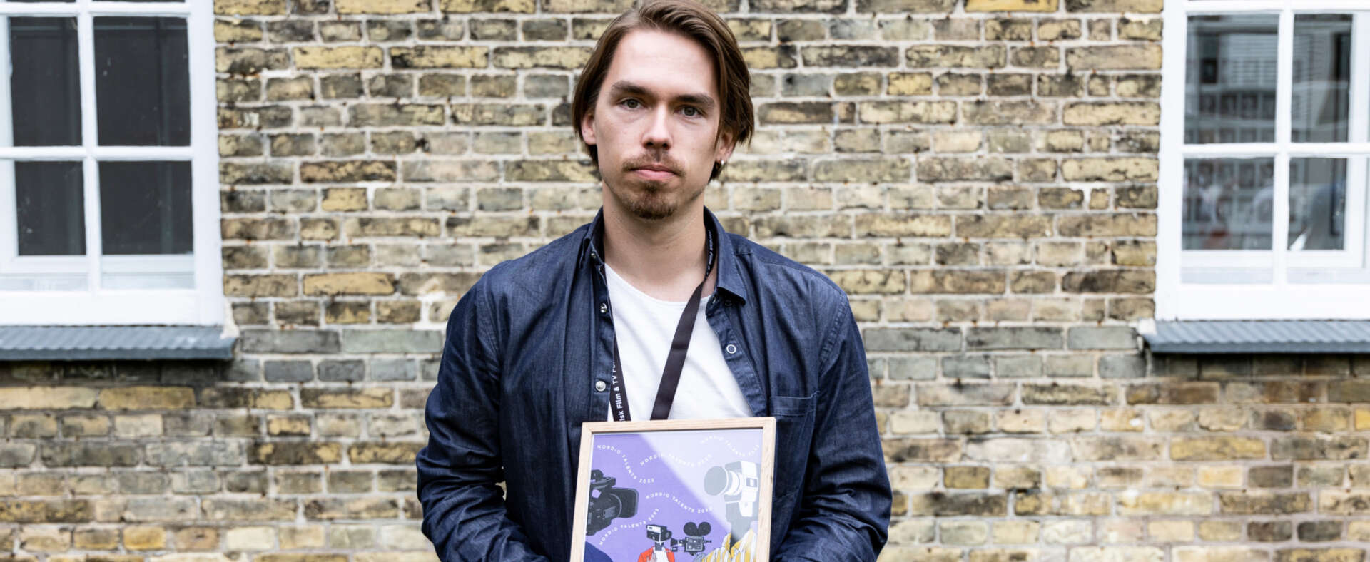 Mies seisoo rakennuksen edessä palkintokirja kädessään
