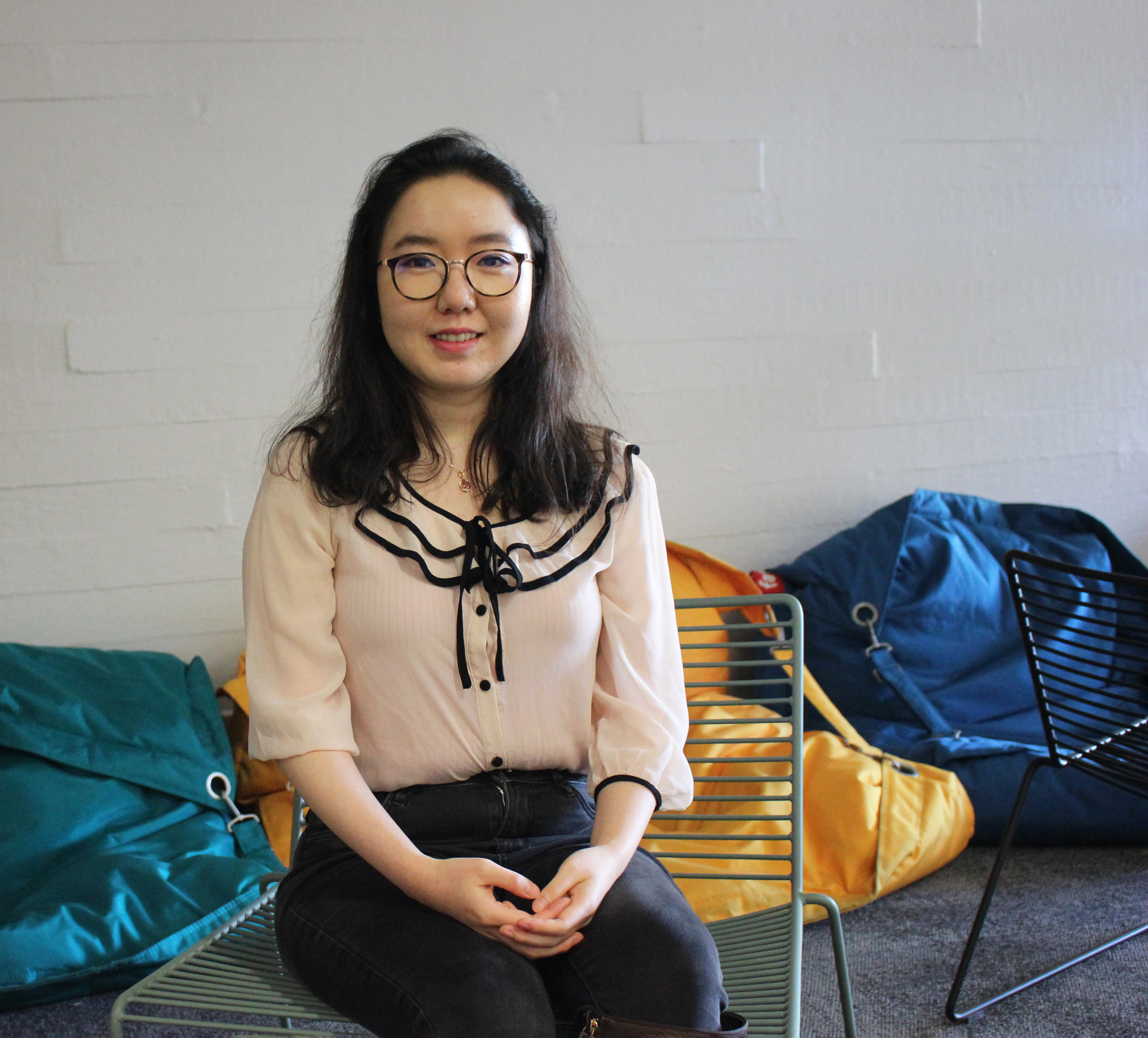 Meishan Lin sitting in a chair at the School of Chemical Engineering lobby. Colourful bean bag chairs in the background.