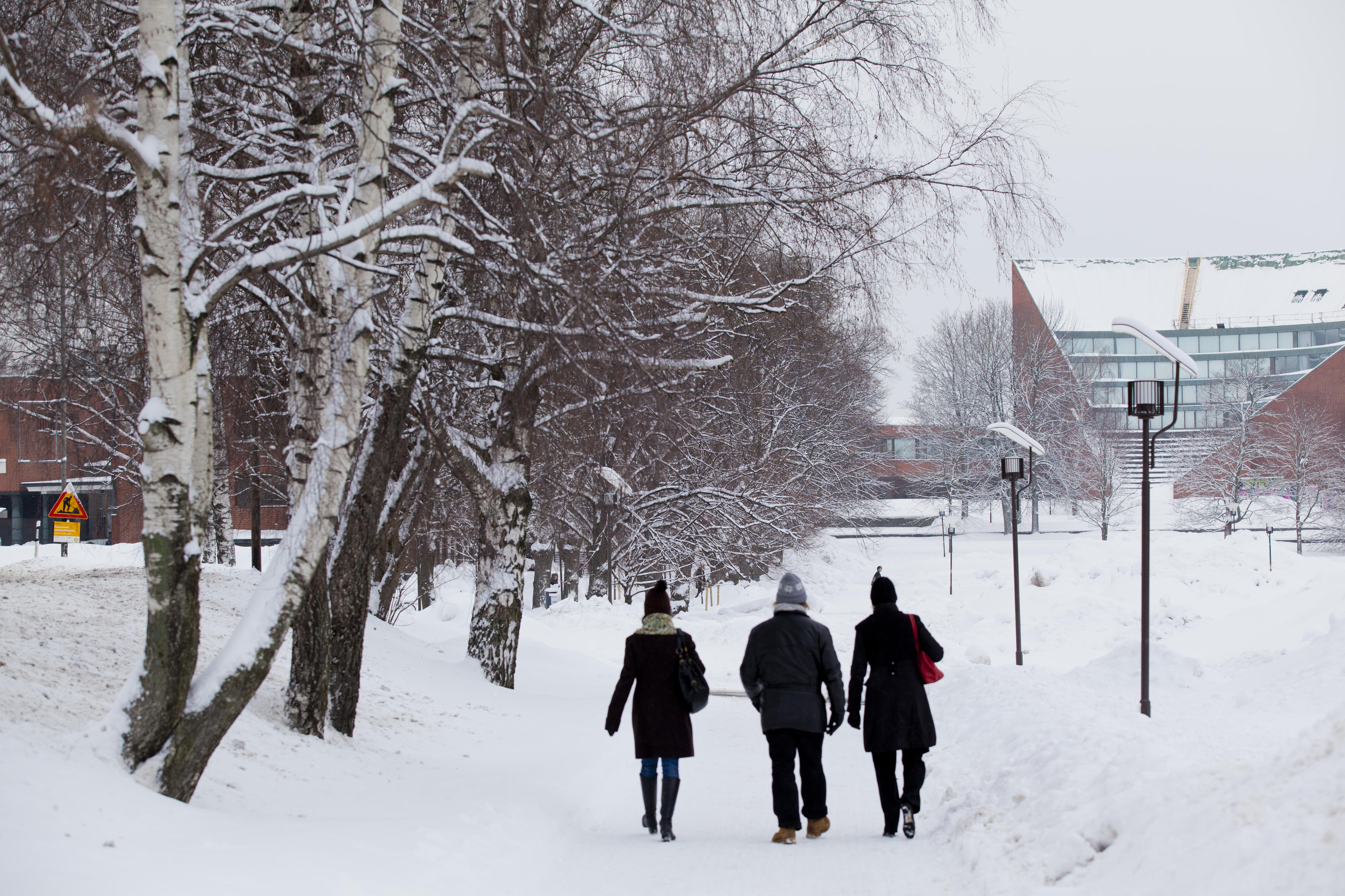 Three people walking on Otaniemi campus on a snowy day. Aalto buildings in the background. Photo: Aalto University / Mikko Raskinen.