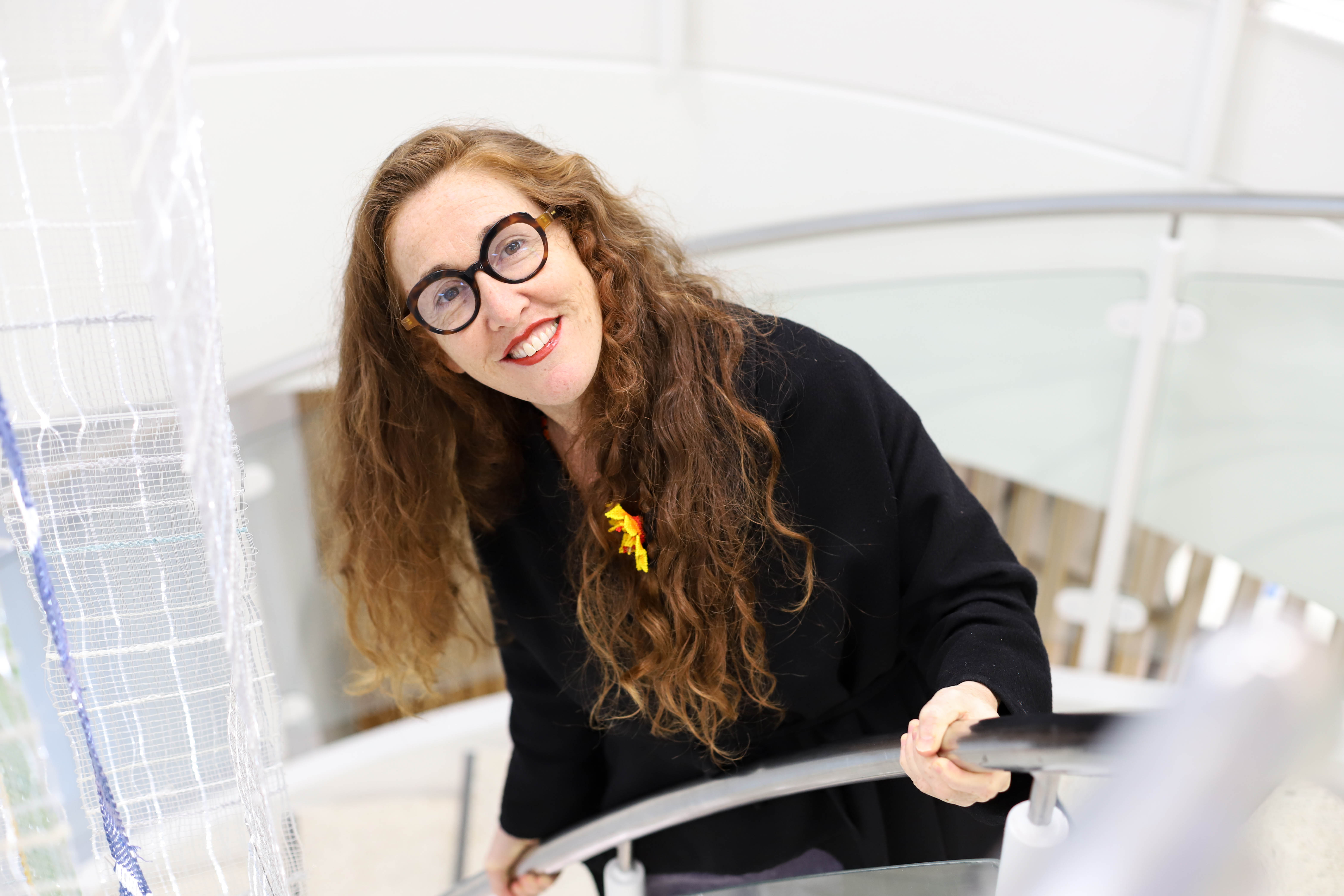 Smiling woman with glasses and long hair standing on the staircase and looking up at the camera