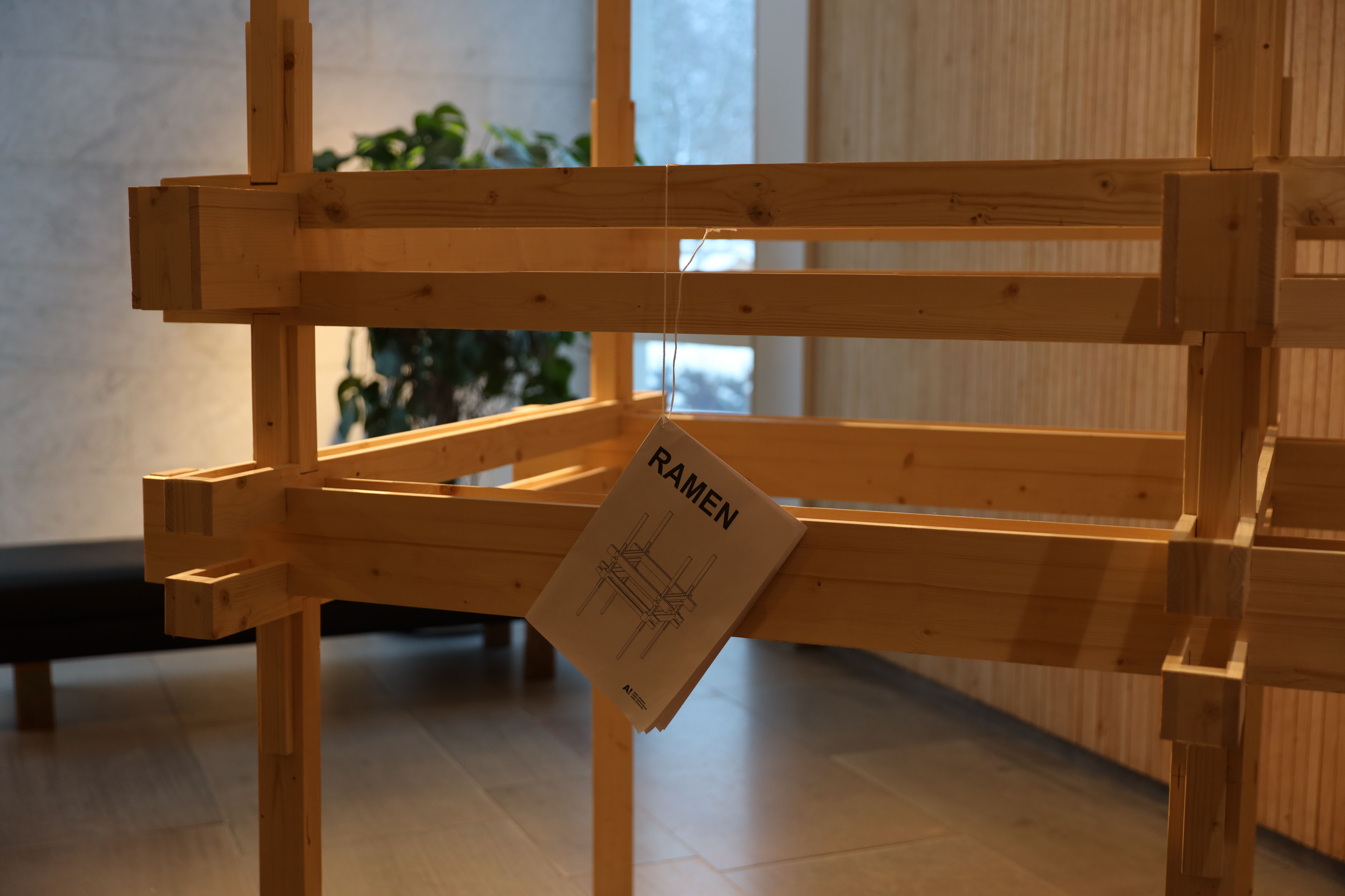 A square wooden frame with a booklet in the style of an IKEA instruction paper, hanging by a piece of string.