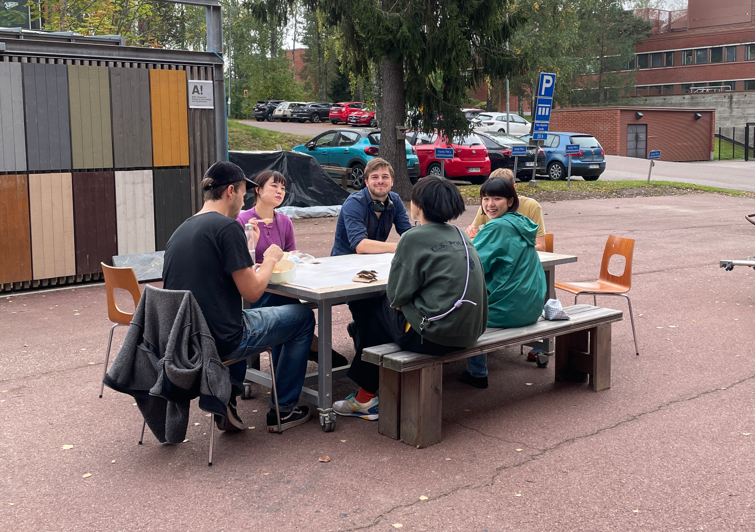 Six students sitting around a table outside enjoying the weather and smiling at camera