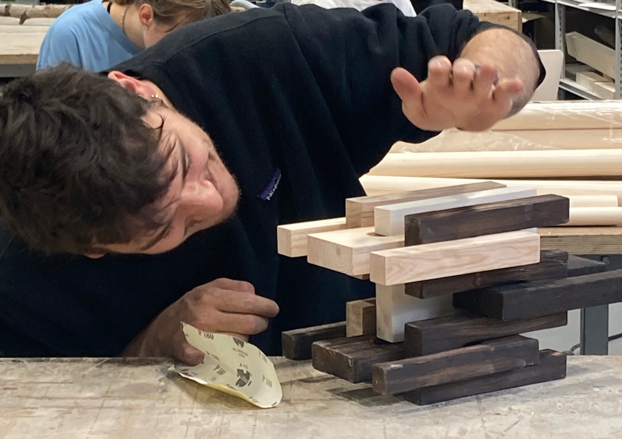 Student working on wooden pieces at a table in workshop