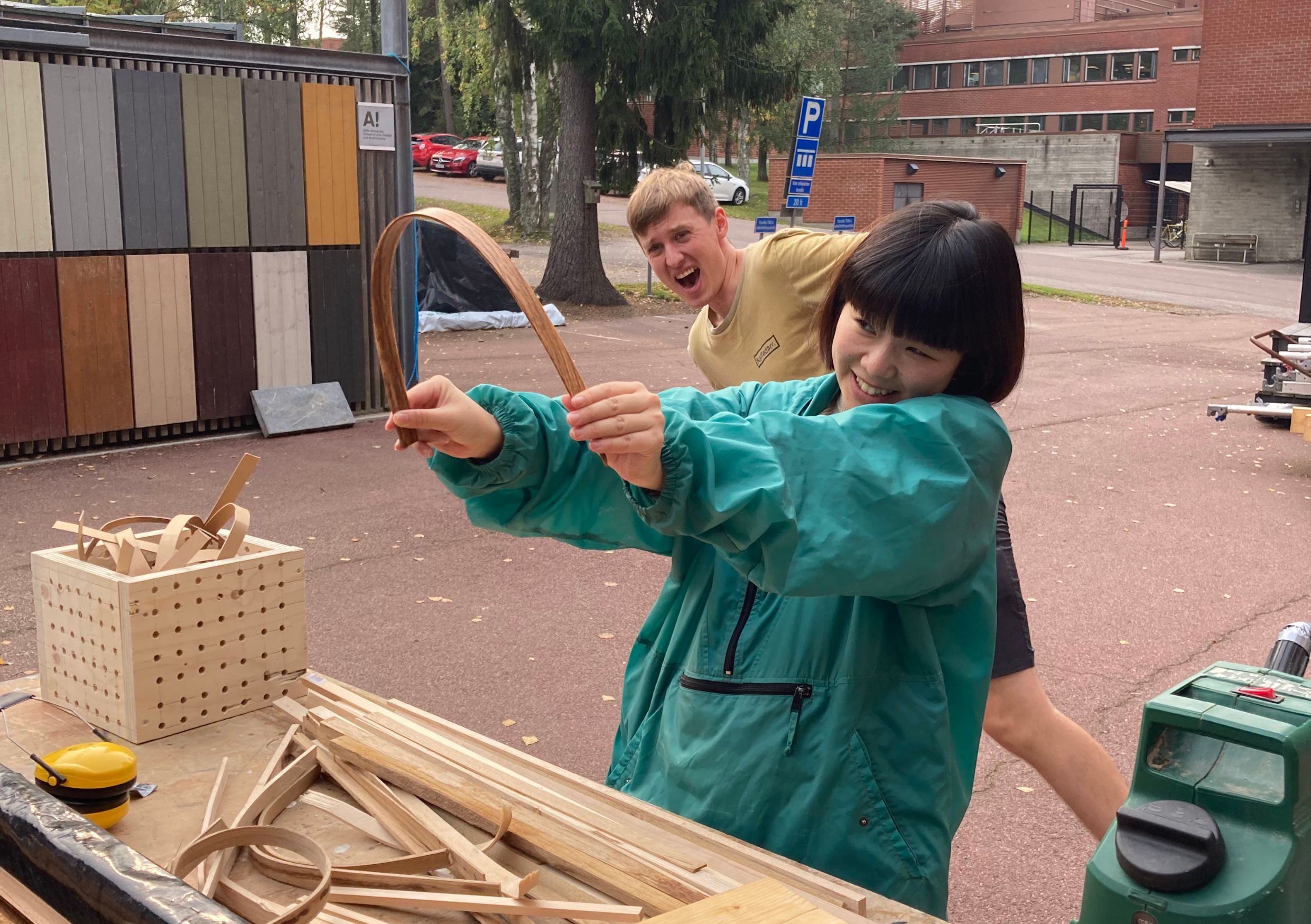 Two students watching tensely as one of them bends a piece of wood to near breaking point