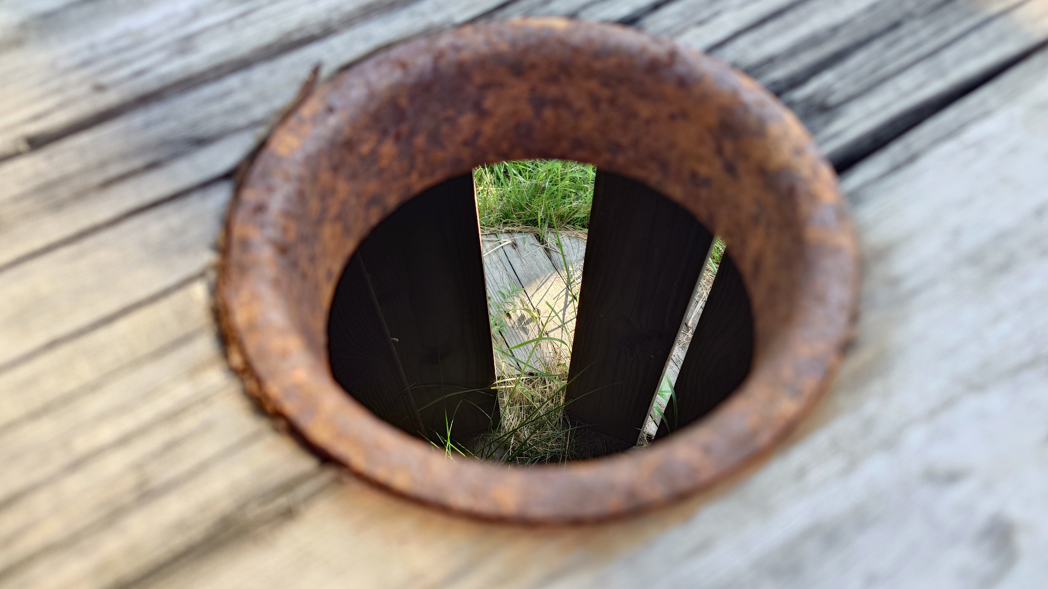 Rusty metal on grey wood, grass can be seen through the hole