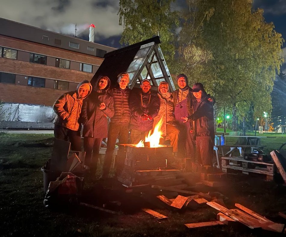 A group of people standing around a campfire.