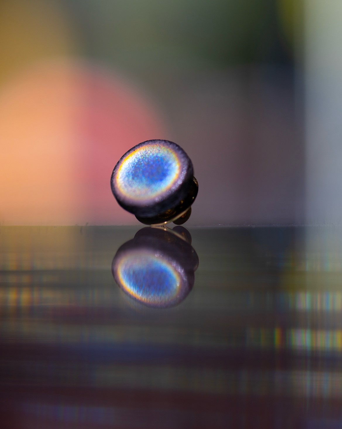 Close-up of a iridescent, round campaign pin reflecting on a shiny surface with a blurred colourful background.
