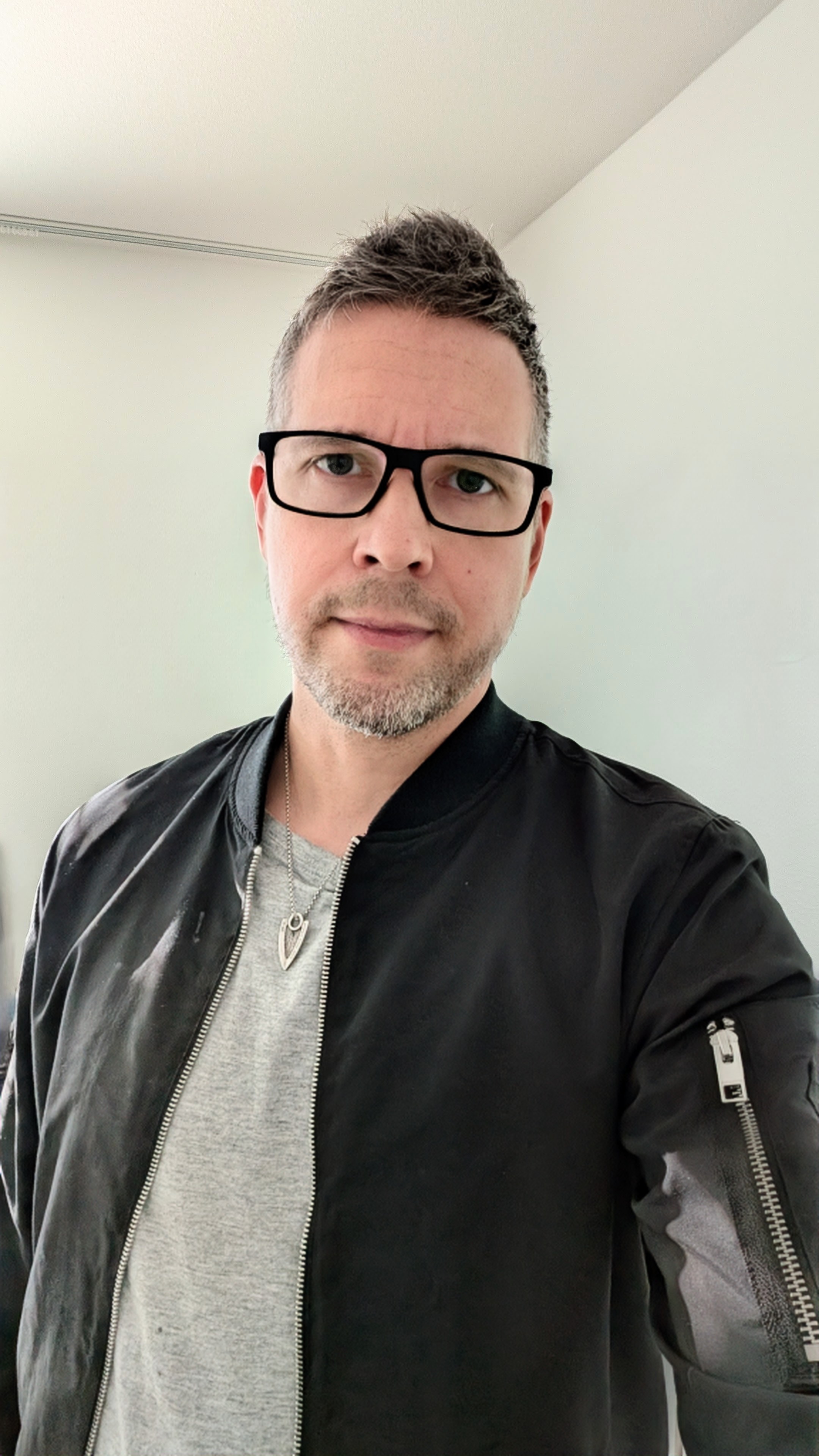 A person wearing a black jacket over a light grey T-shirt, with a silver necklace.
