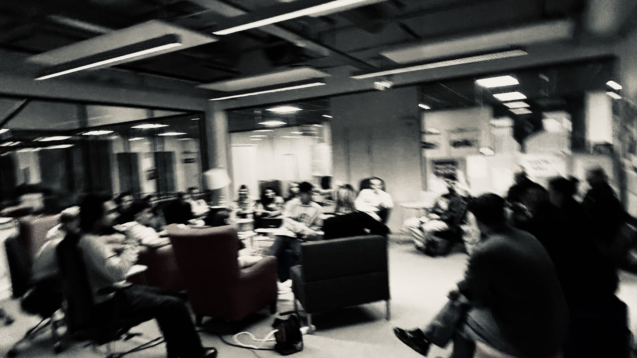 A blurred image of a group of people sitting and discussing in a modern office space with glass walls.