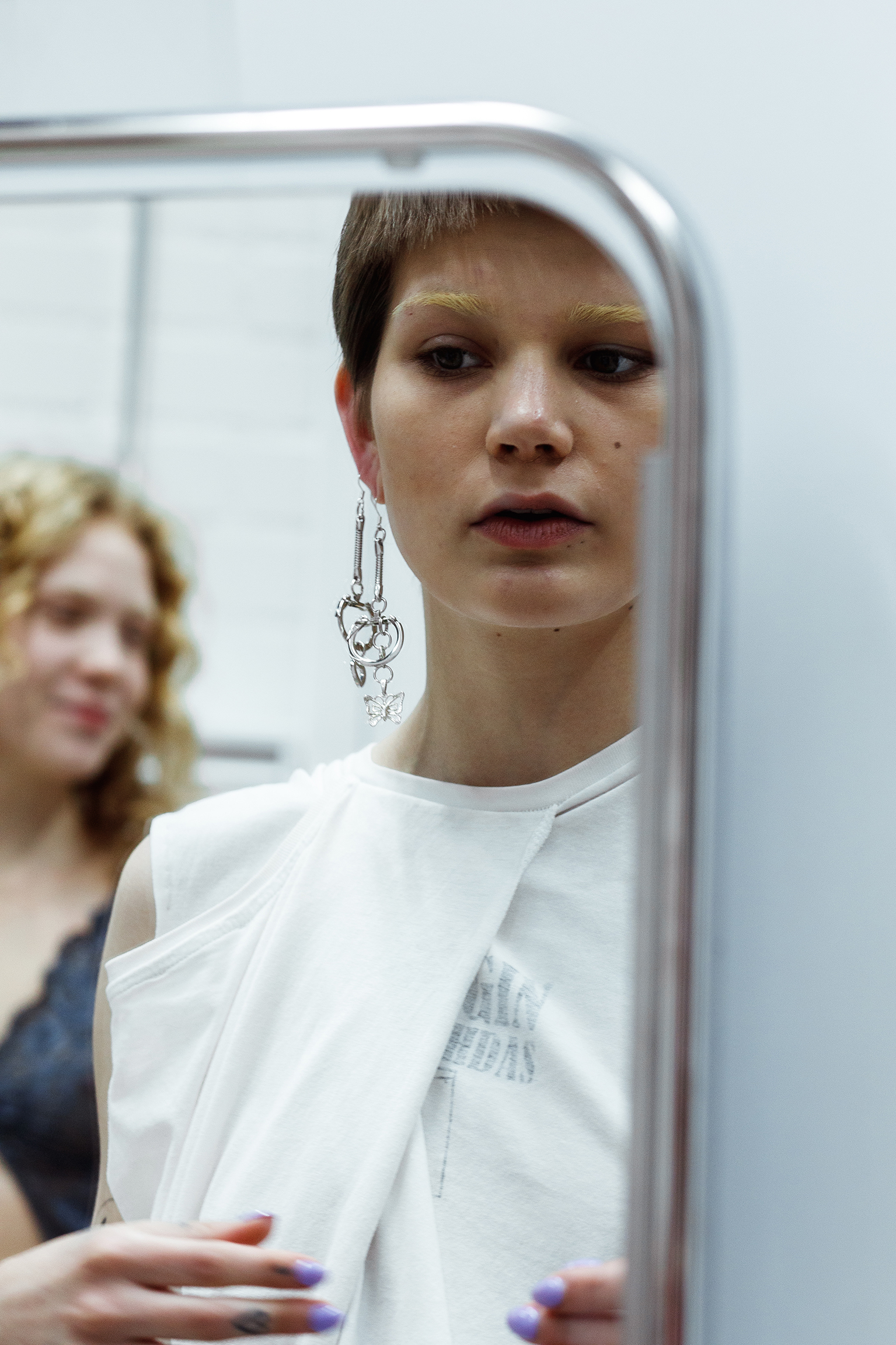 Person wearing a white shirt and large silver earring, with another person in the background.
