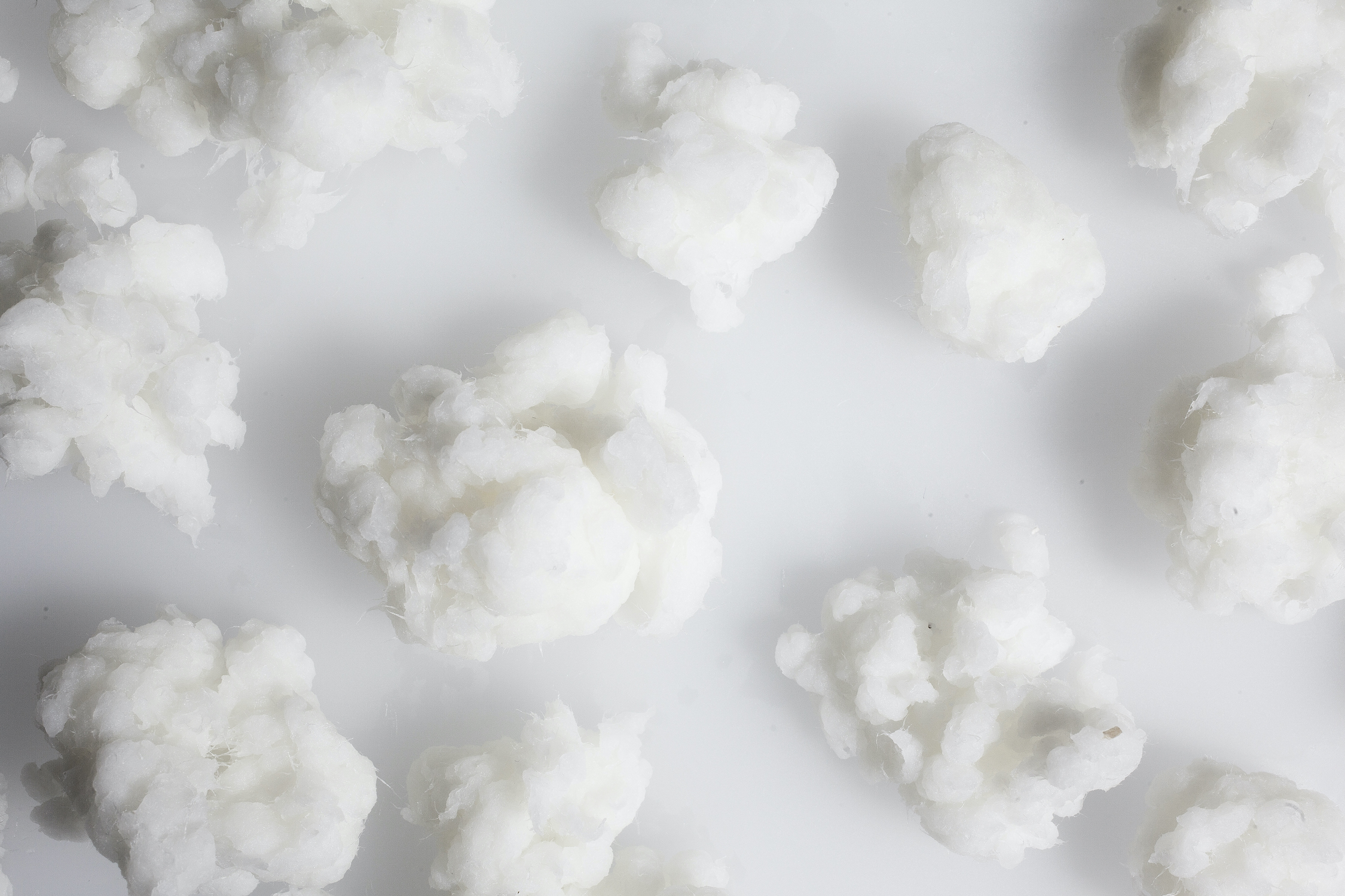 Several white cellulose fibre balls resembling cotton balls on a white surface.