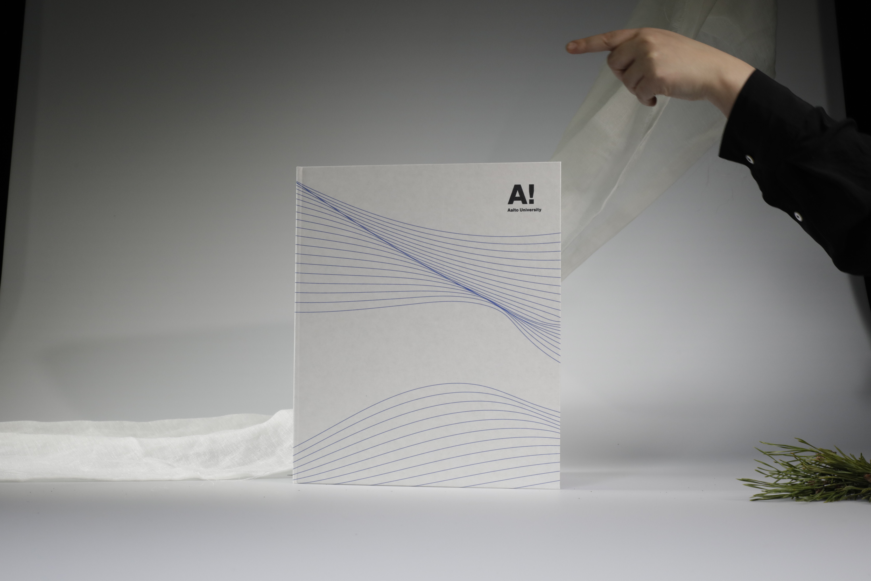 A hand revealing a white Aalto University folder with blue lines on a white background.
