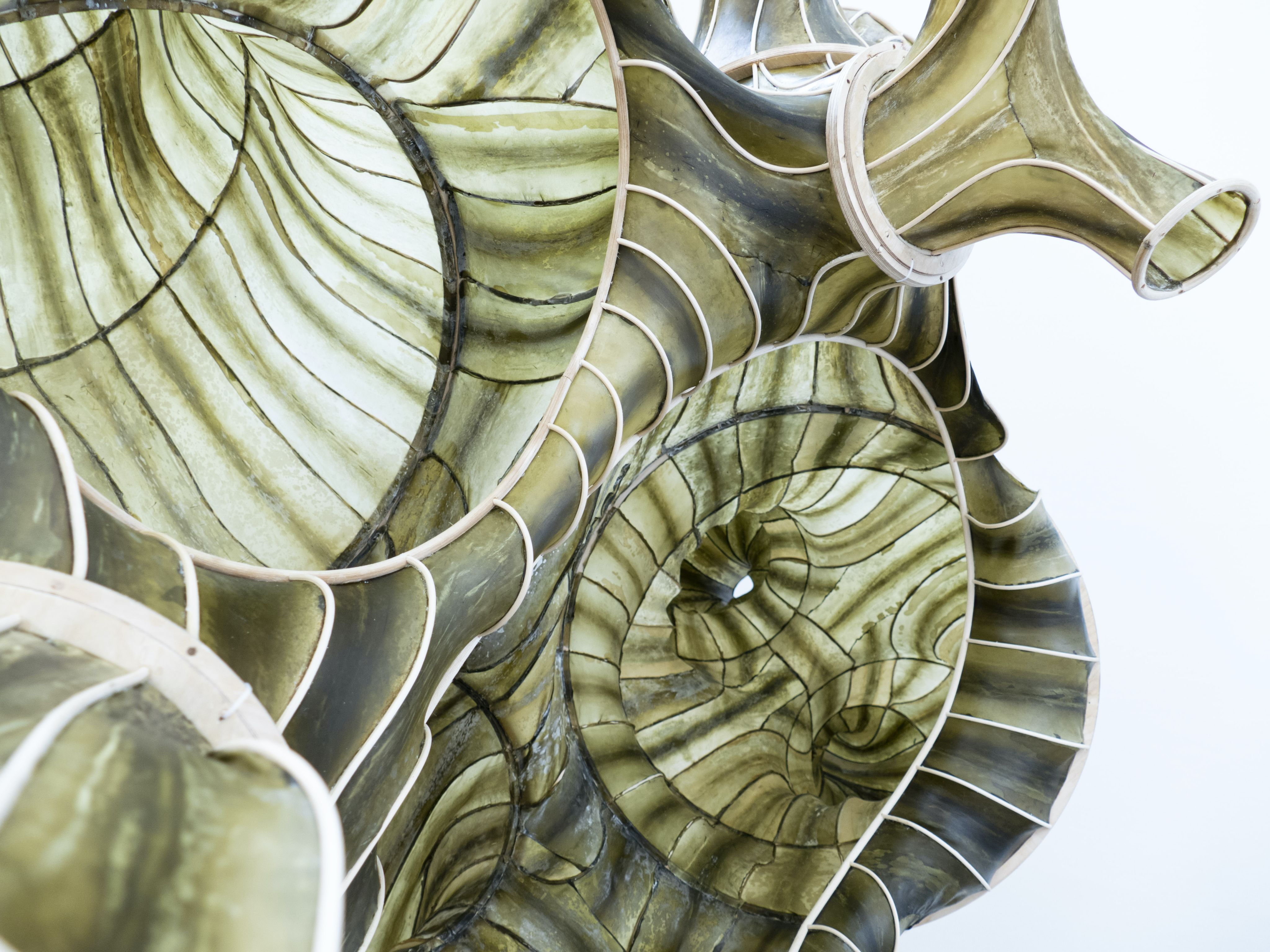 Close-up of a large, green, spiral-shaped sculpture resembling a seashell with intricate patterns and white borders.