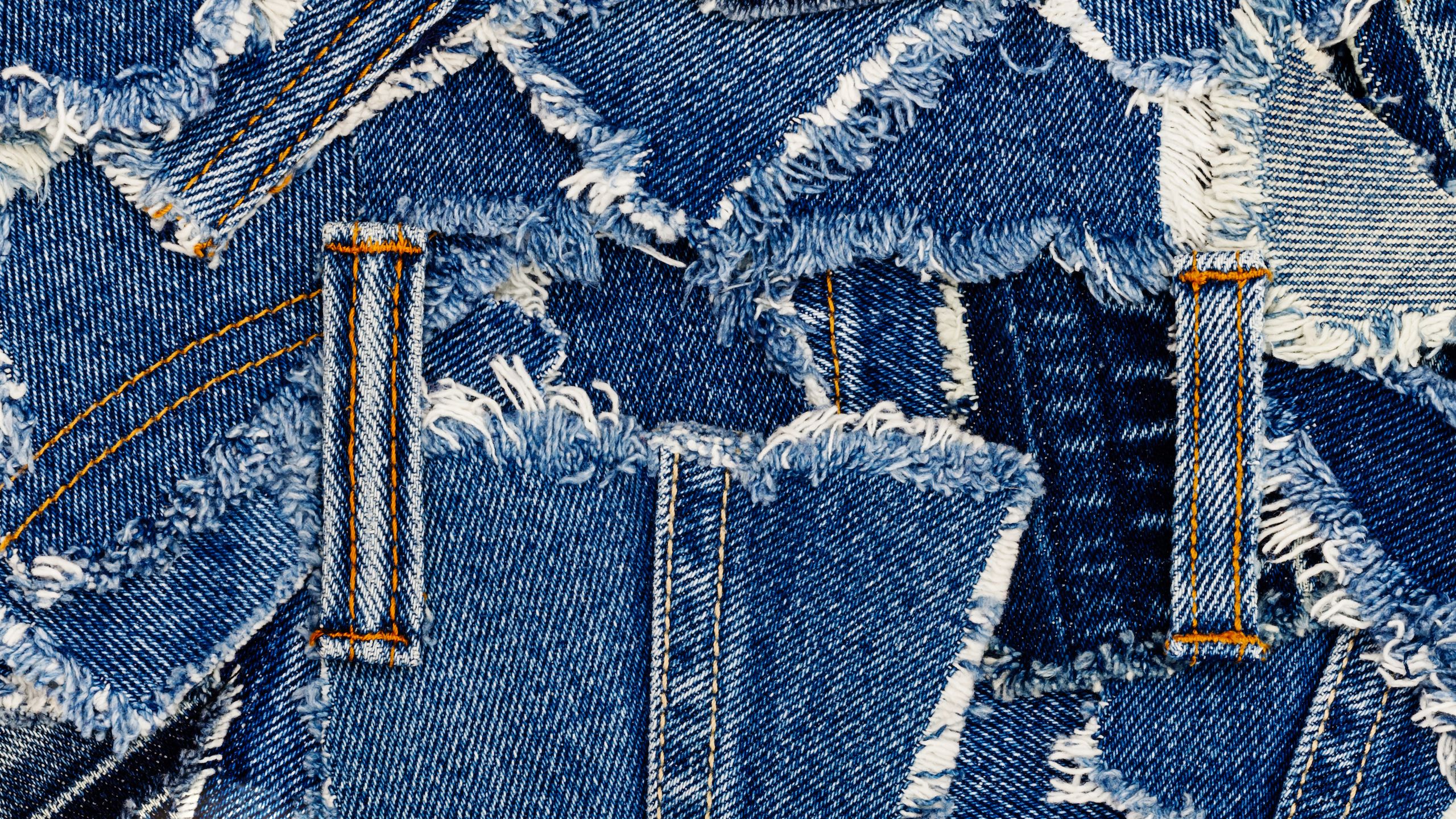 A collage of various blue denim fabric pieces with frayed edges and visible stitching.