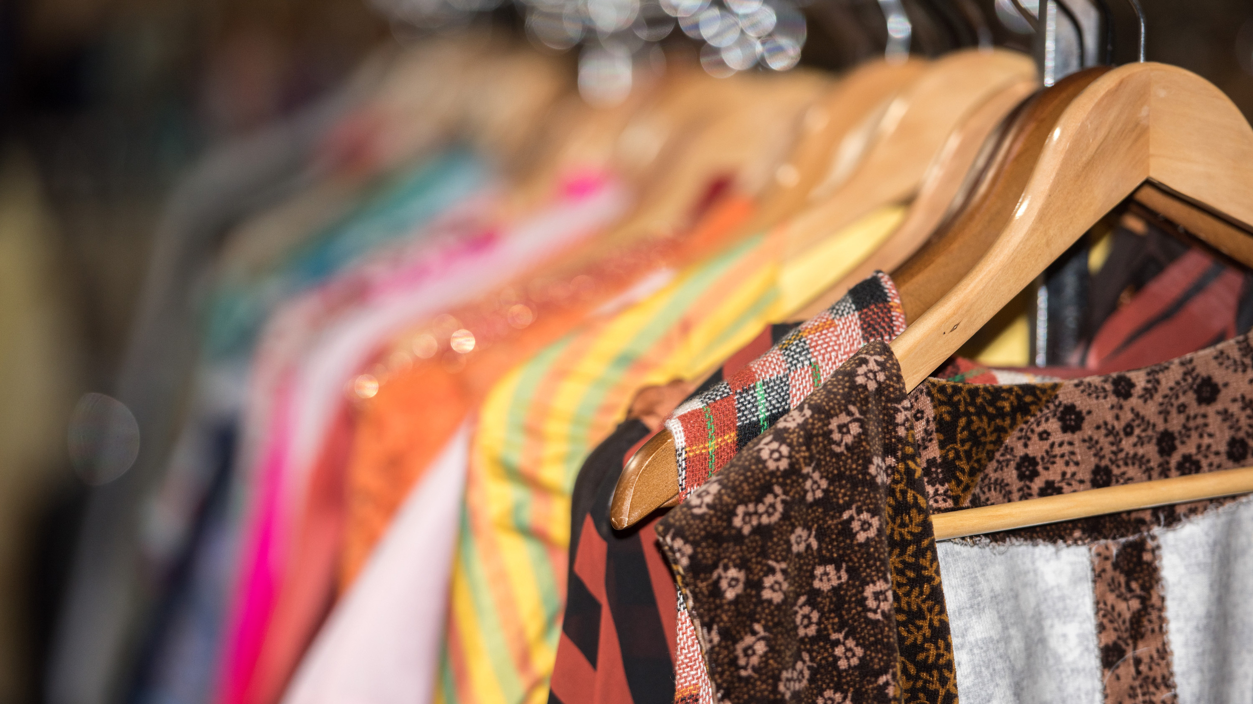 A row of colourful clothes on wooden hangers in a shop. Patterns include stripes, florals, and checks.