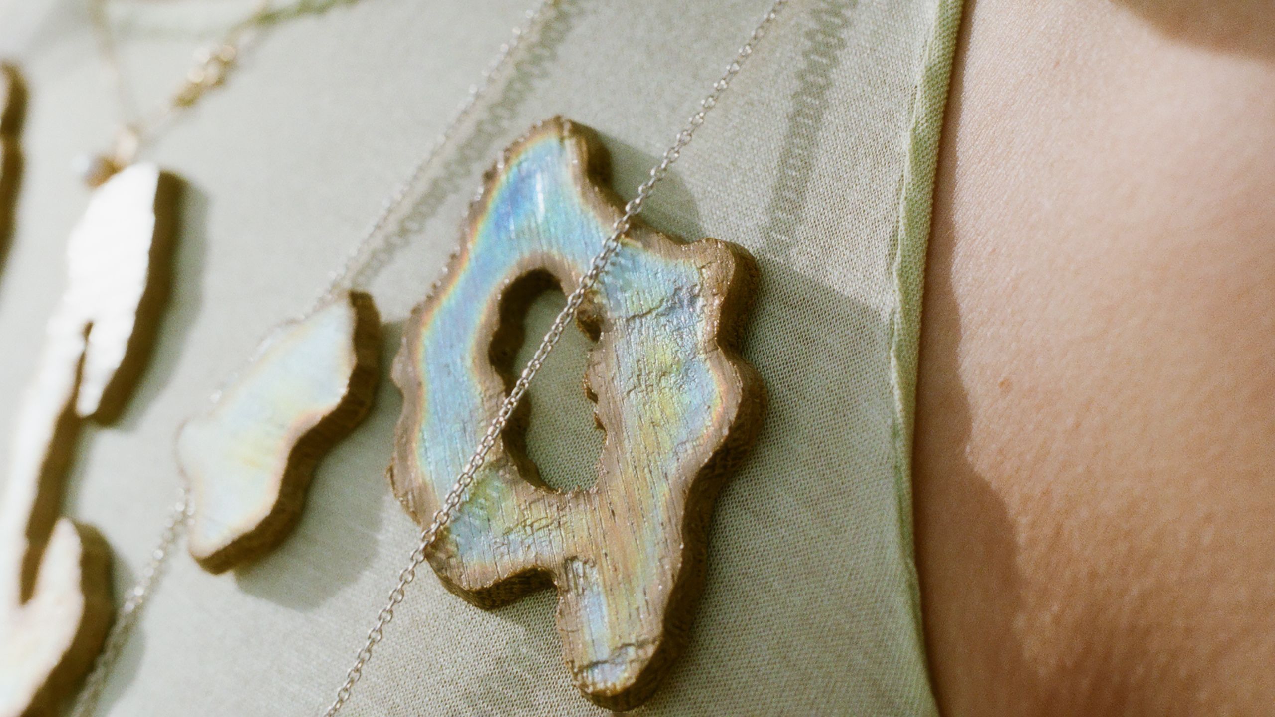Close-up of a person wearing necklaces with iridescent wooden pendants on a light green fabric.