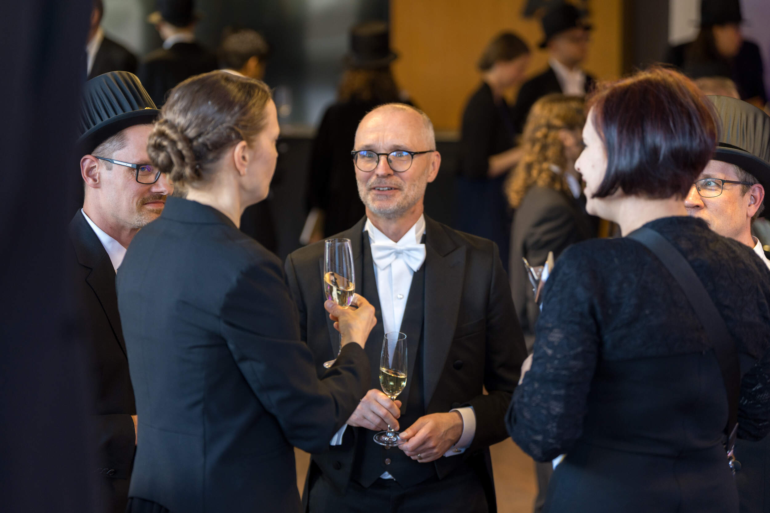 People in formal black suits and top hats chatting and holding champagne glasses at a reception
