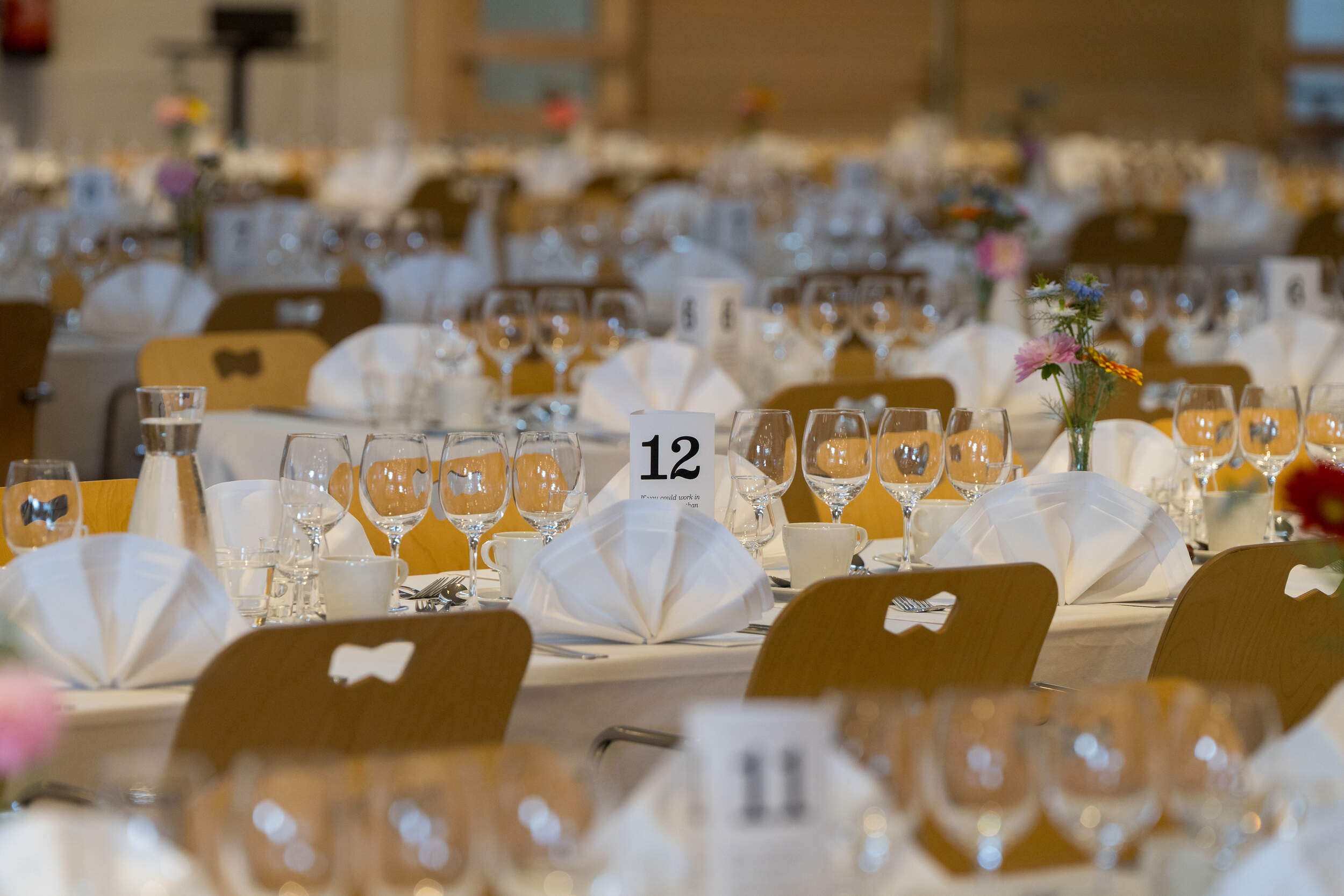 Elegant banquet hall with white table settings, glasses, flowers and table number 12 in focus