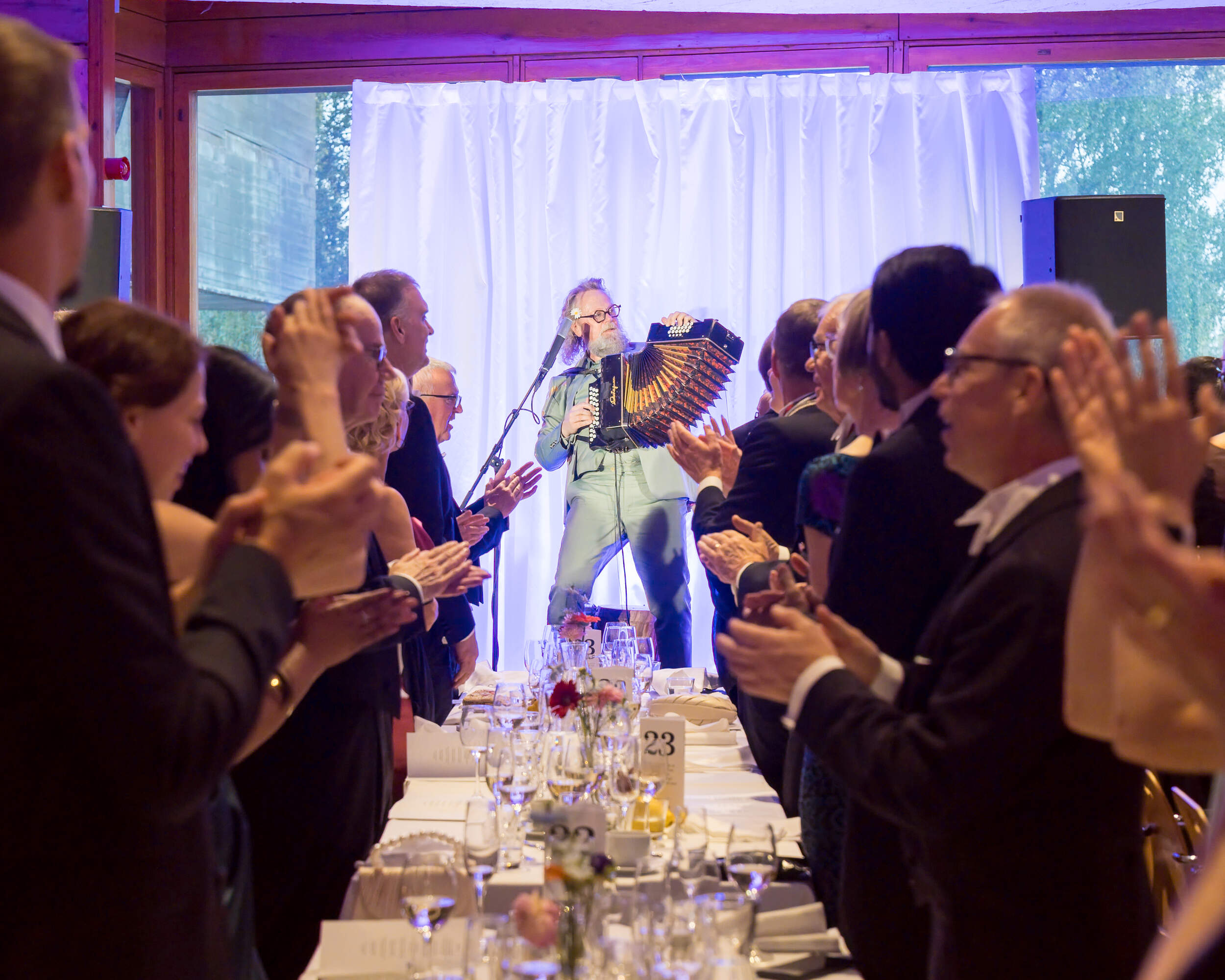 Accordionist performing on stage as formally dressed dinner guests stand and applaud at long tables