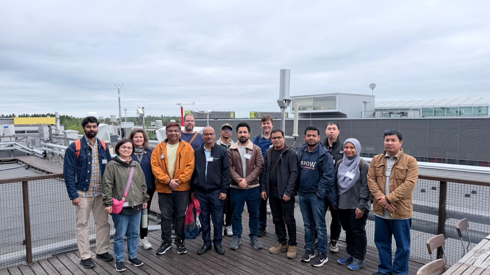 Group of people posing on a rooftop terrace with industrial buildings in the background under cloudy sky