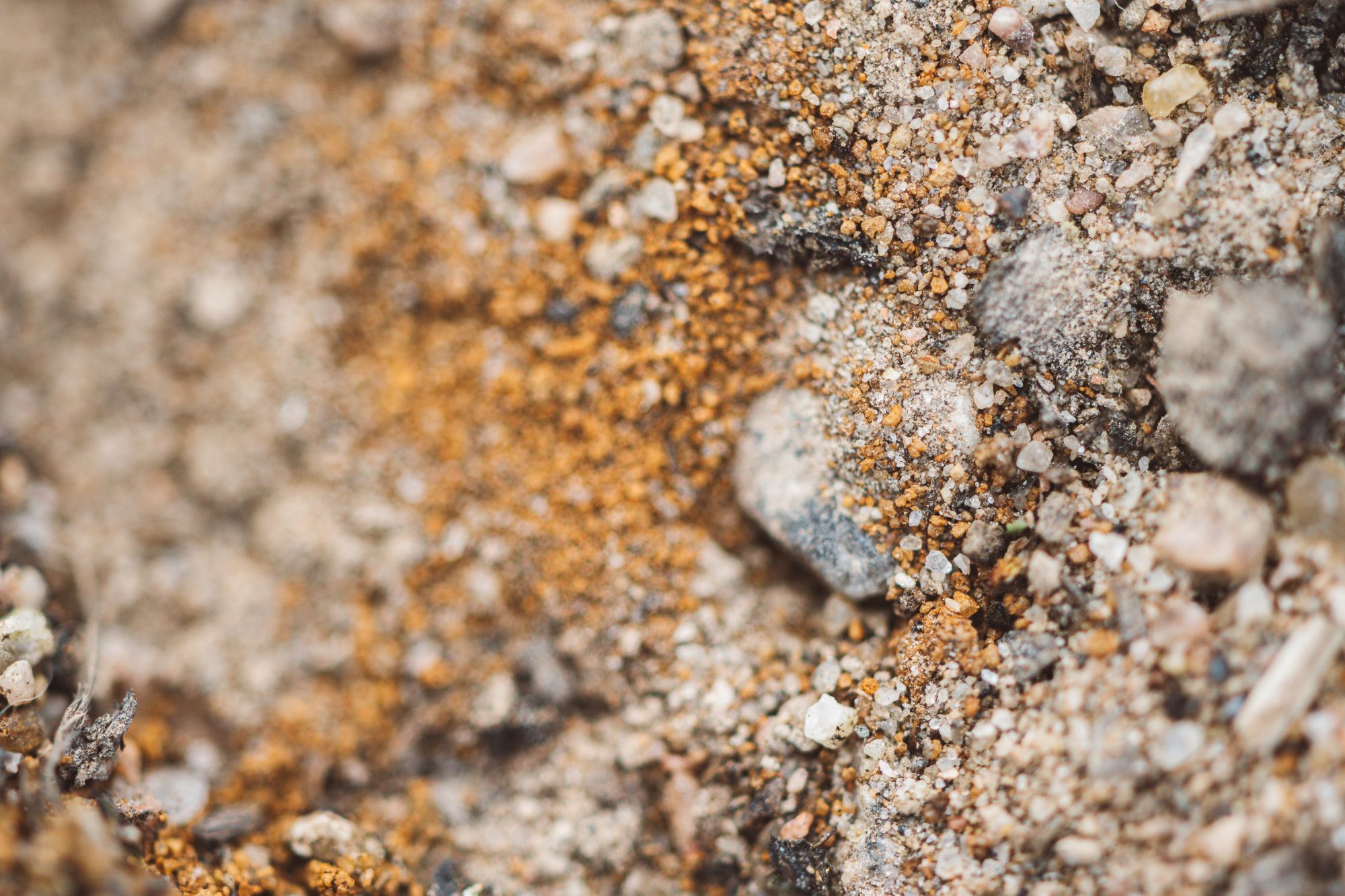 Close-up of coarse sandy soil with small stones in beige, orange and grey tones