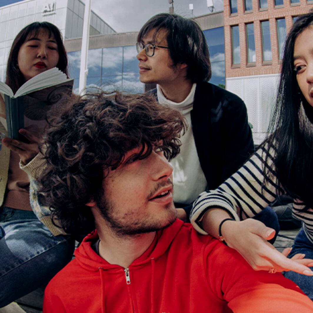 Four Aalto University students sitting outside with a book