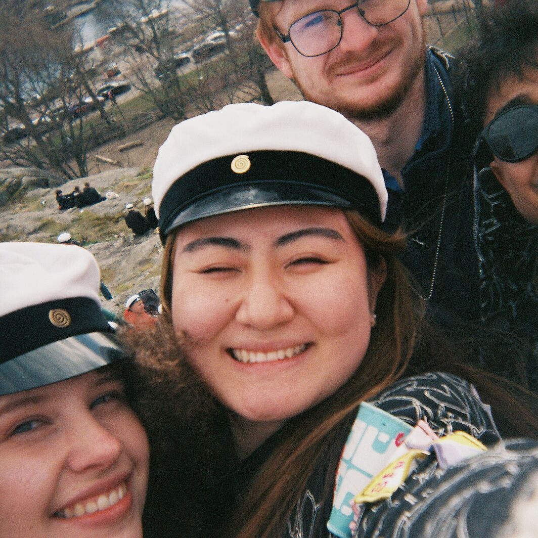 Group of people wearing white caps with black bands. The background shows a park with trees and a waterfront.