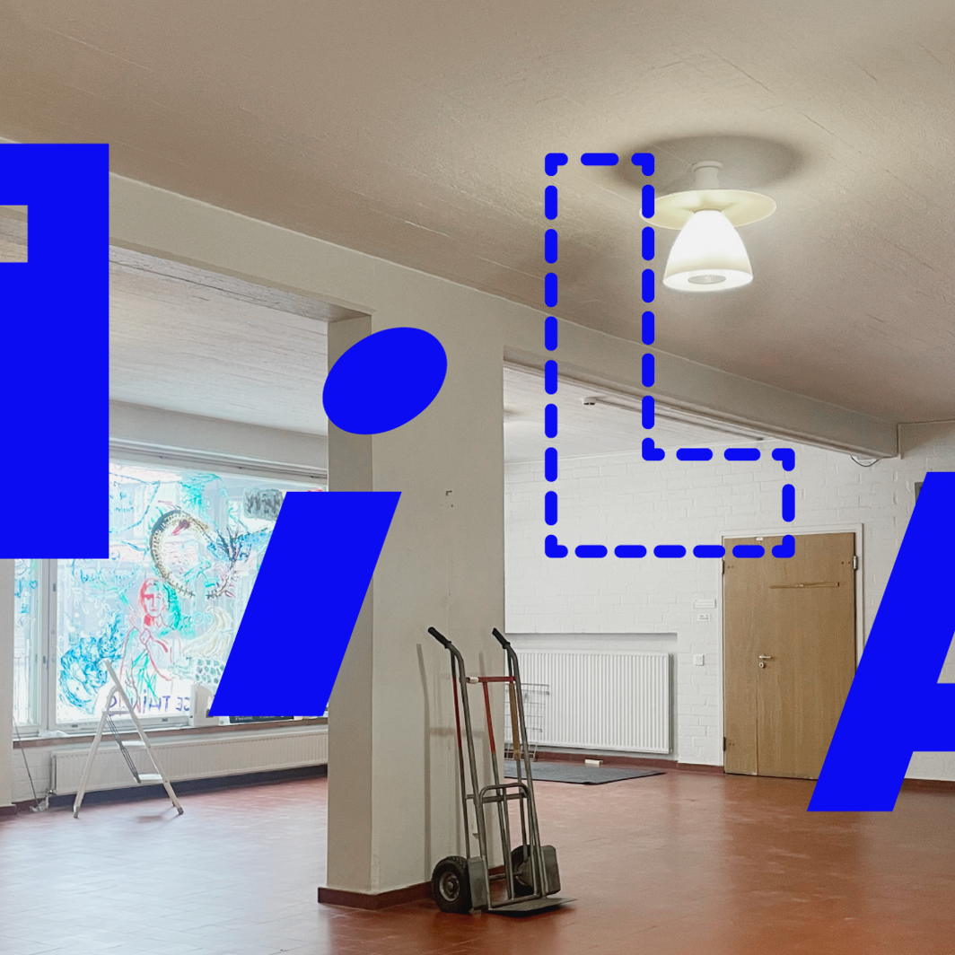 Tyhjä sisätila, punainen lattia, valkoiset seinät, nokkakärryt ja suuri sininen teksti ”TILA!”