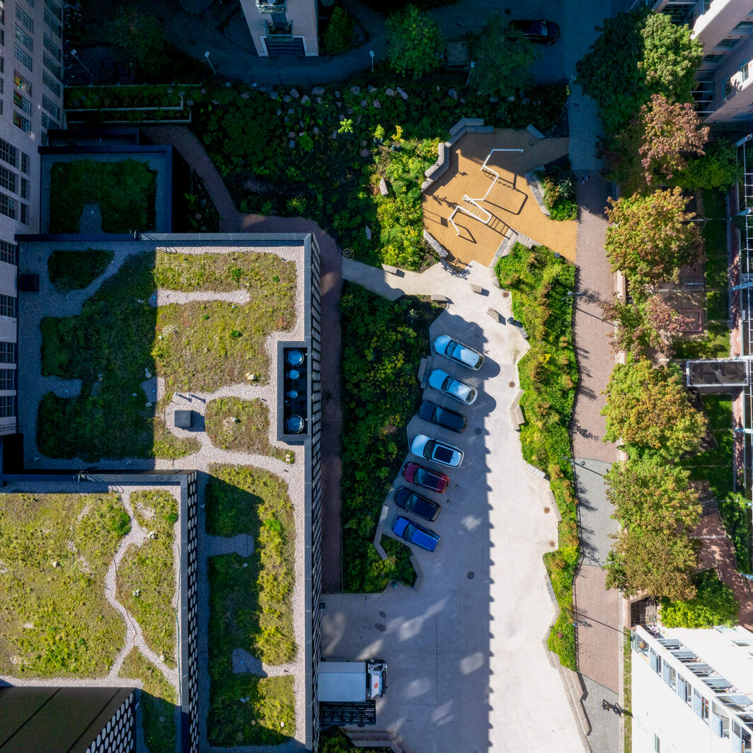 Aerial view of two tall buildings, green roofs, parked cars and a small playground between them