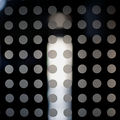 Lasipaneeli, jossa tasaisesti riveissä ja sarakkeeissa harmaita pisteitä, taustalla epätarkat valonlähteet.
