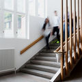 Several people walk down a staircase inside a building with large windows and vertical wooden beams.