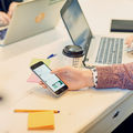 Close-up on student searching information on their mobile phone at a table with laptops