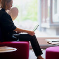 Person sitting on a pink couch in front of a big window holding a laptop