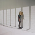 Still from the film Like Shadows Through Leaves, 2021. A figure stands next to a minimalist wall wearing a cardboard bird mask