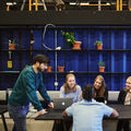 Students sitting around a table with laptops and discussing.