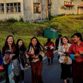 Nine students wearing bright colours carrying notebooks walking down a street with buildings in the background