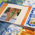 An illustrated book with model wearing summery outfit lays on colourful textiles surface