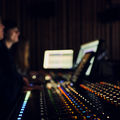 Two people seated next to an audio mixer
