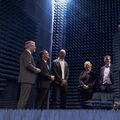 Group of people in a room with blue soundproofing panels, standing around a tall antenna structure.
