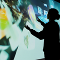 AI generated vision of a teacher interacting with virtual screens in a dark room, with colourful digital images projected on the walls.