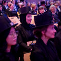 People wearing academic dress and traditional black hats, seated in rows at a formal event.