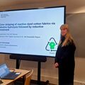 A woman presenting her master's thesis on textile chemistry at Aalto University. A laptop and notes are on the table.