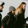 Three people in winter clothing walking outdoors on a snowy day. One holds a coffee cup.