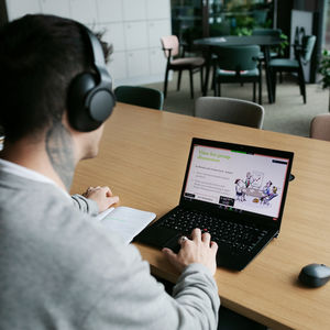 Man with headphones sitting with his back to a camera, looking at a computer screen that says "Time for group discussion".